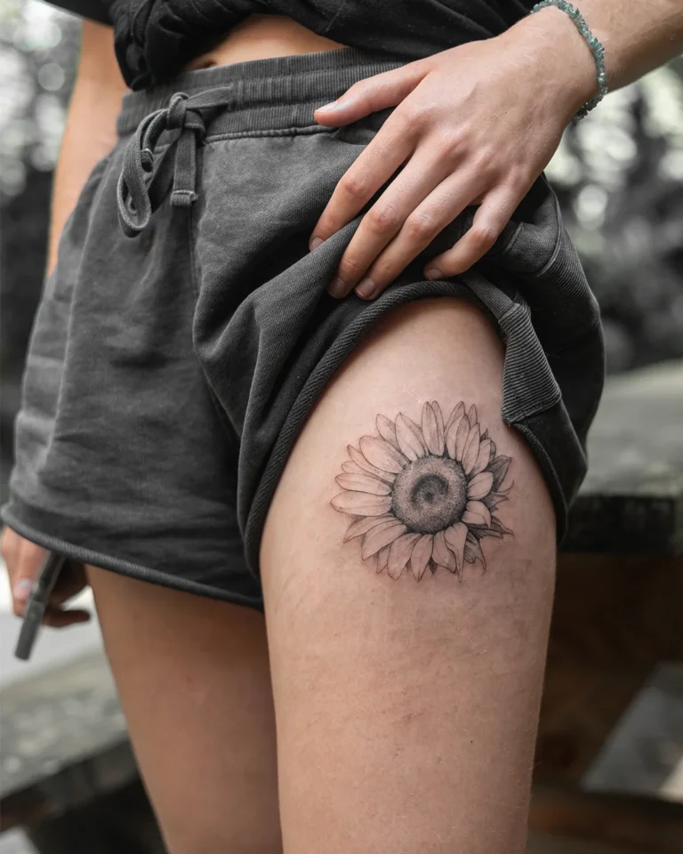 fine line tattoo van een zonnebloem op een bovenbeen vrouw