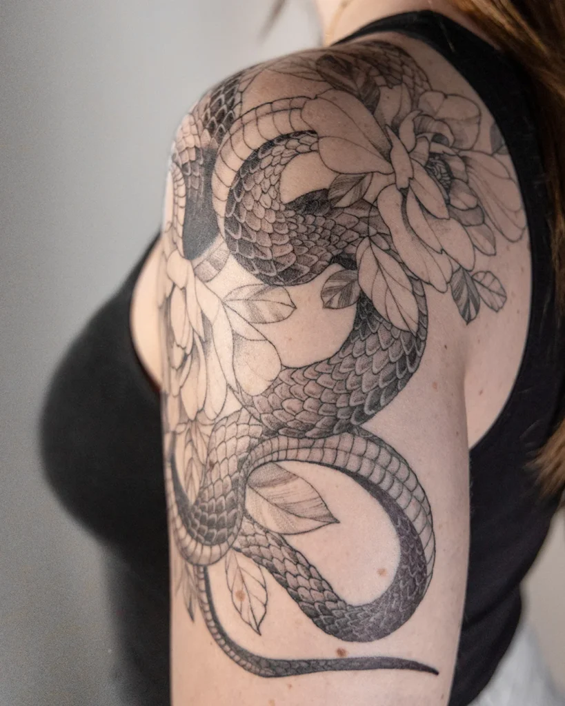 slang met bloemen fine line tattoo schouder vrouw