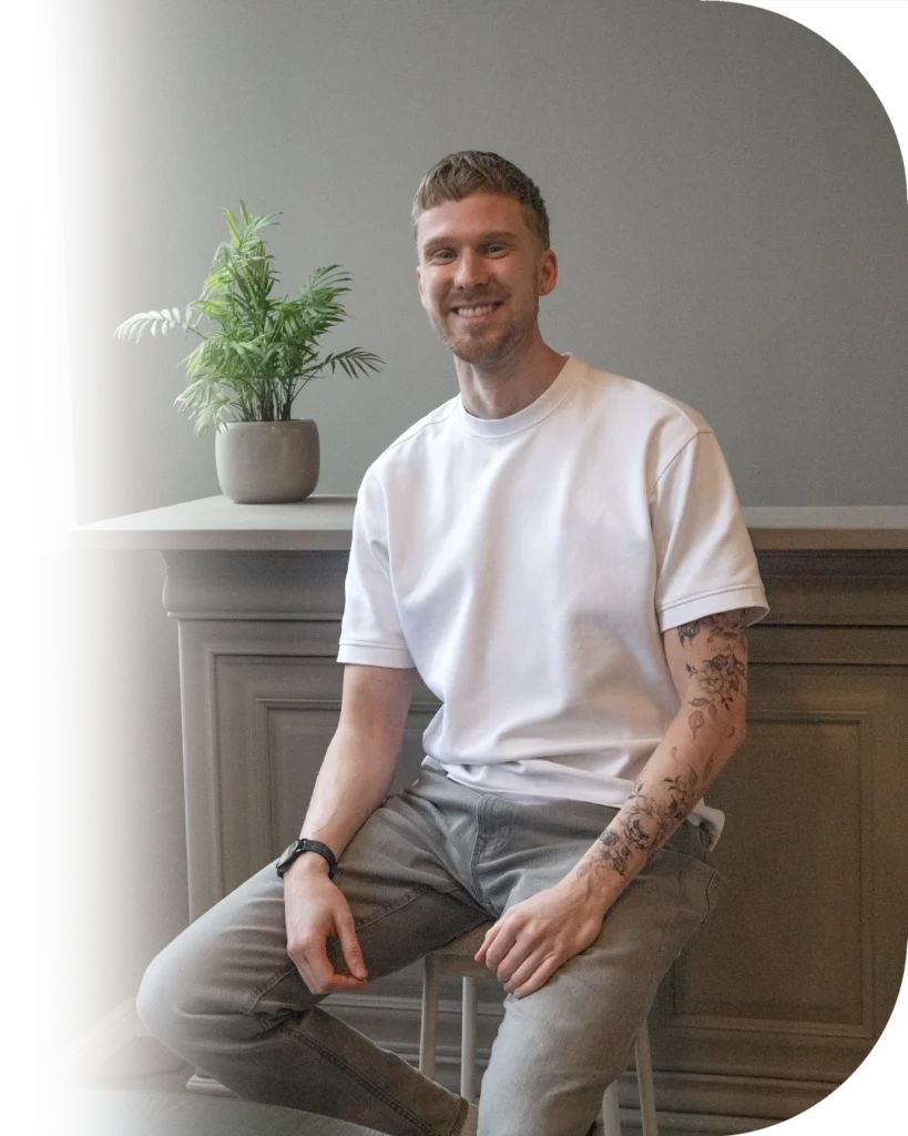 Tattoo artiest Cas Bakker op de foto gezet op een krukje voor een kast met daarop een kleine plant.